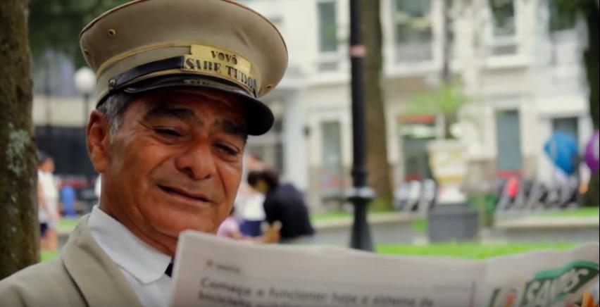 Motorneiro de bonde lendo jornal em praça. Imagem para Santos Eu te Amo. #paratodosverem