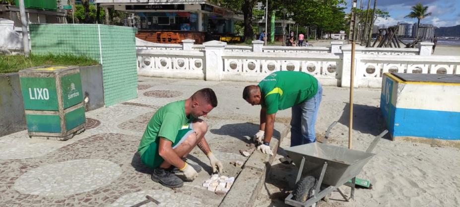 dois homens uniformizados fazem reparos em mosaico português no calçadão interno da orla. #paratodosverem 