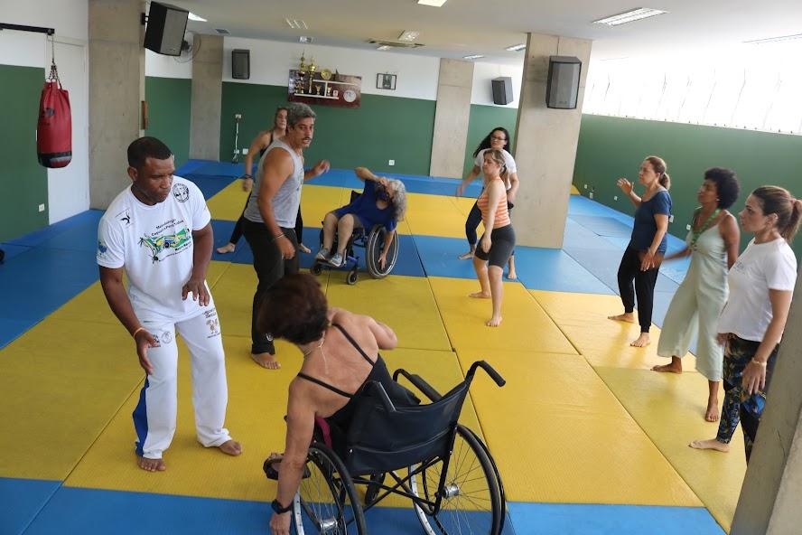 Cadeirantes e mulheres em pé realizam atividade. #paratodosverem