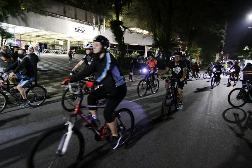 ciclistas estão pedalando pela rua à noite. #paratodosverem