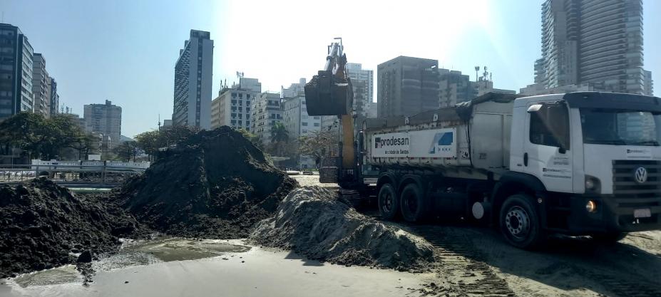 caminhão está parado na faixa de areia e escavadeira ao fundo remove volume de areia de dentro do canal. #paratodosverem