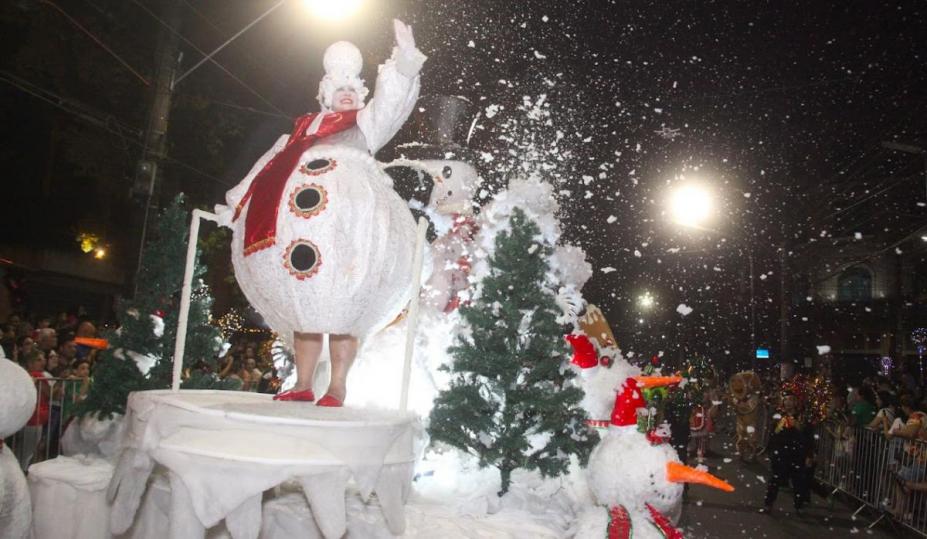 carro alegórico com personagem de boneco de neve. Há 'neve' flutuando no ambiente. #paratodosverem