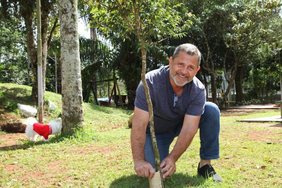 Homem planta muda de árvore em jardim olhando para a câmera. #paratodosverem