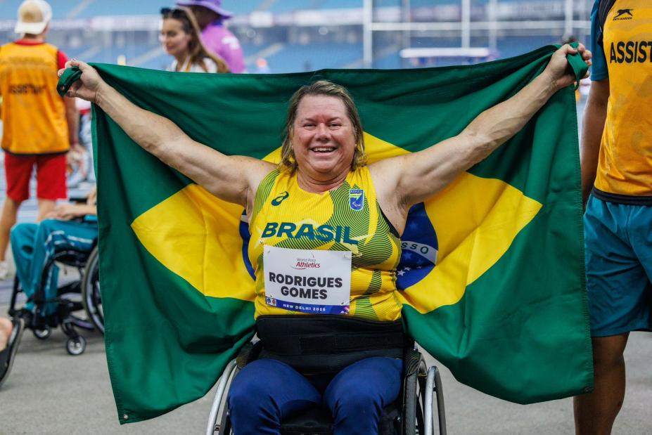 a atleta de braços aberto segurando a Bandeira do Brasil. #paratodosverem