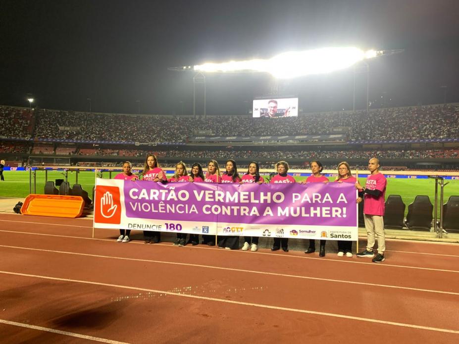 mulheres seguram faixa em estádio de futebol. #paratodosverem