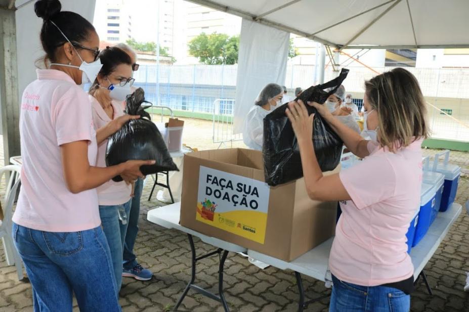 Mulheres colocam doação em caixa de papelão no posto de vacinação #paratodosverem