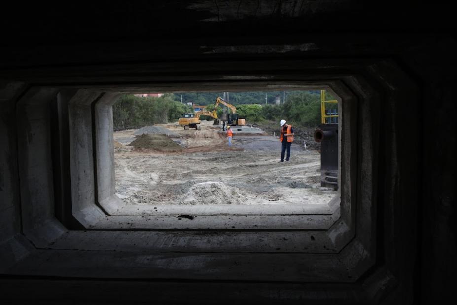 fotógrafo se posicionou na entrada de aduela para fazer dela uma moldura e mostrar a sua proporção em relaão ao homem e máquinas que estão no fundo. #paratodosverem