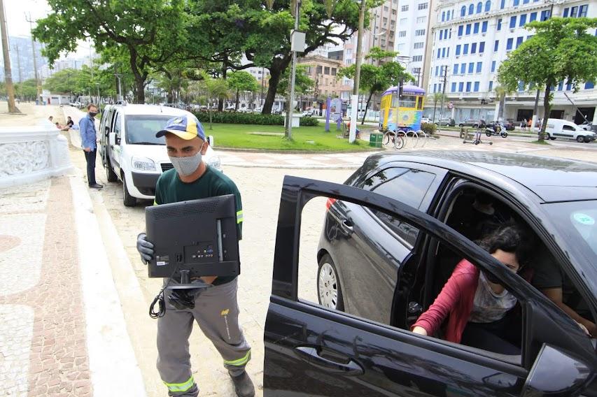 Homem carrega monitora doado por mulher dentro de veículo preto. #pracegover