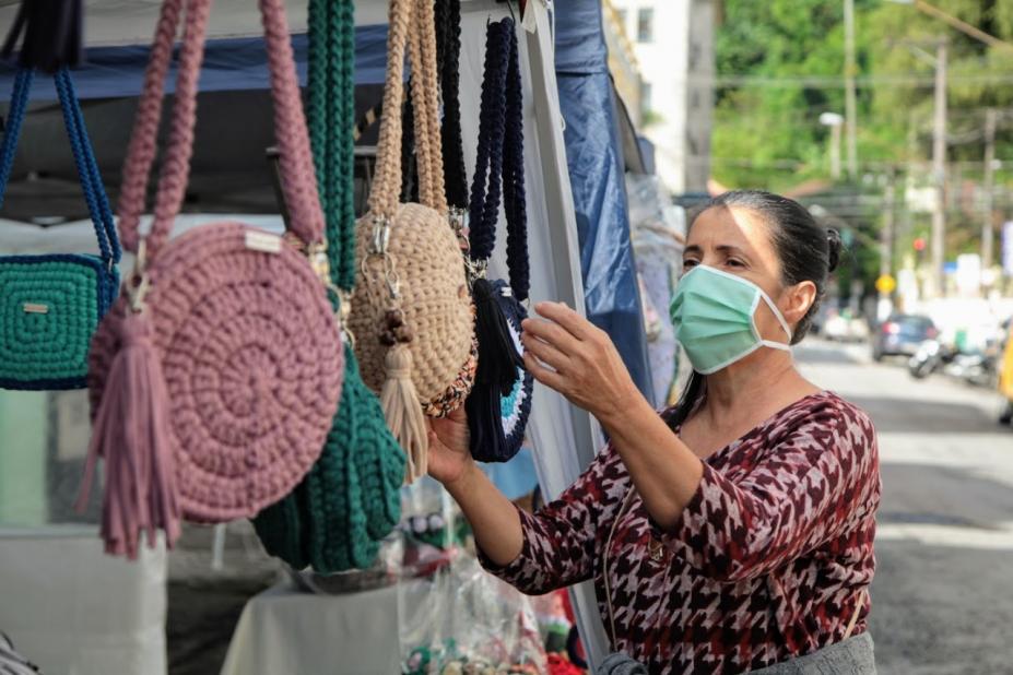 Mulher mexe em bolsas de crochê em uma barraca #paratodosverem