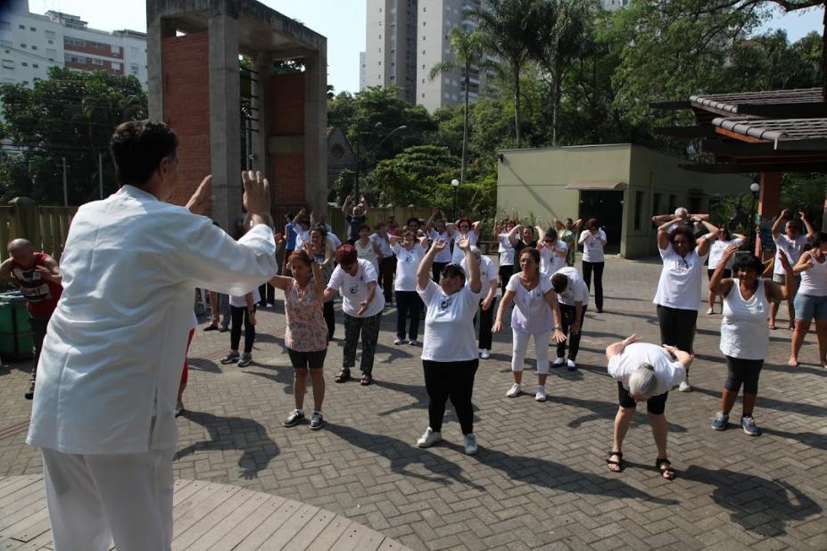 aula de tai chi chuan com professor de costas para imagem fazendo movimento que é repetido pelos alunos à frente. #paratodosverem 