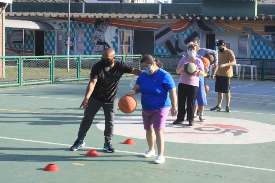 professor está orientando menina que bate bola de basquete. A quadra está com marcações por onde ela tem que ultrapassar. #paratodosverem