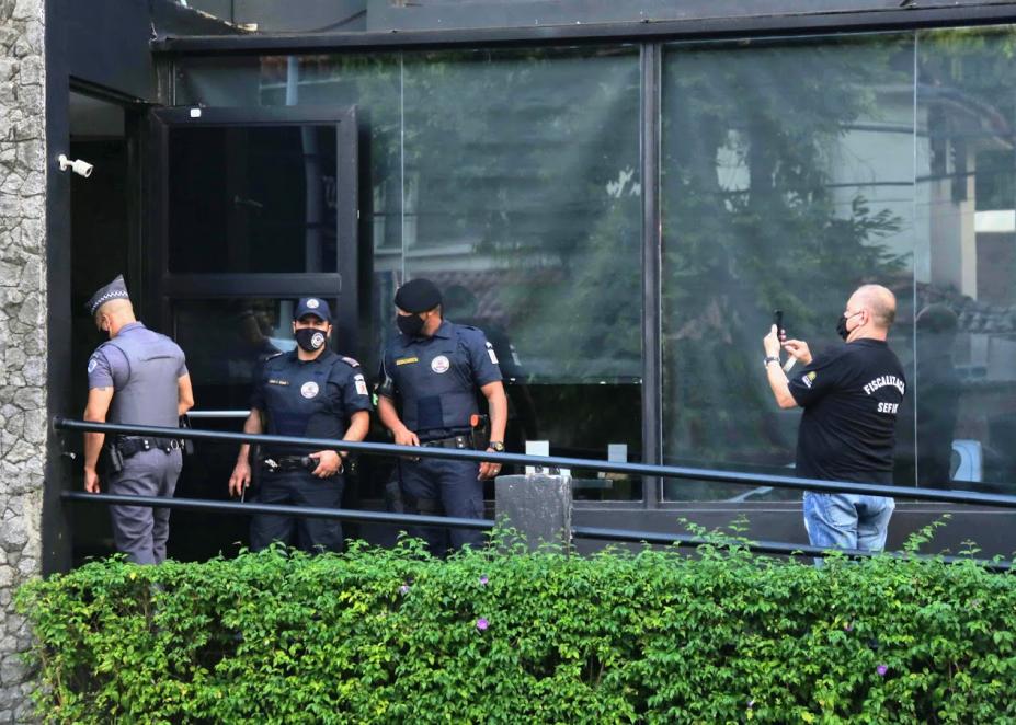 Guardas municipais, policial militar e fiscal estão na porta de estabelecimento.#paratodosverem