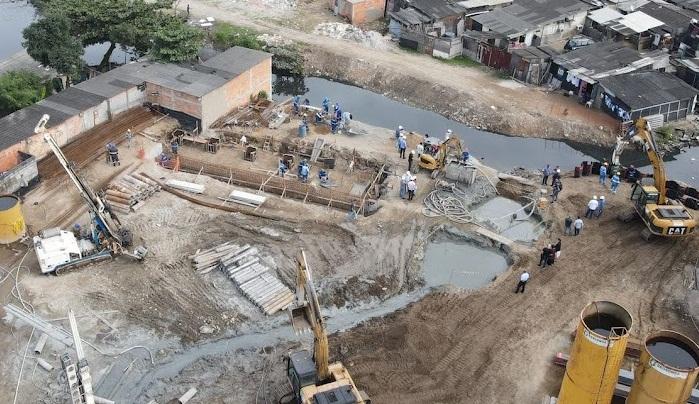 vista aérea e geral do local das obras. Há guindastes operando. Grandes buracos na terra. Homens trabalhando. #paratodosverem