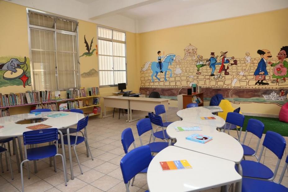 Interior de classe com pintura artística nas paredes. Mesas e cadeiras. #paratodosverem