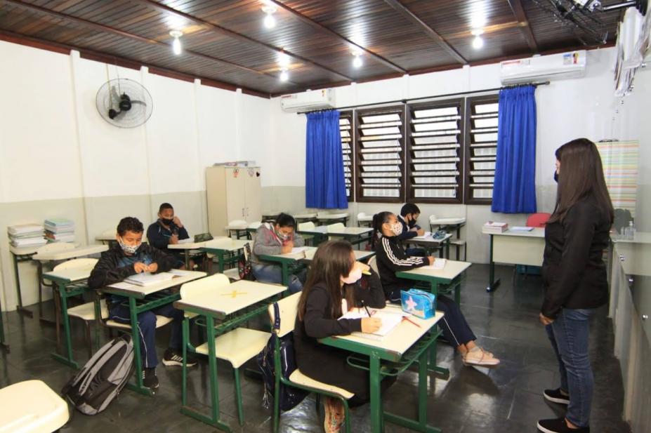 alunos estão sentados em carteiras. Professora na frente de todos. #paratodosverem