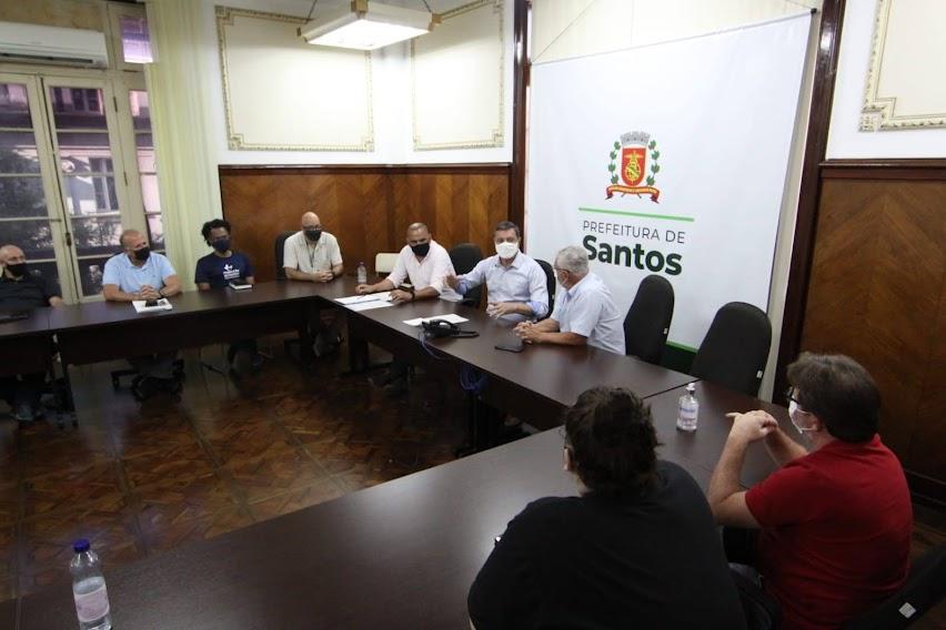 Pessoas conversam sentadas em uma mesa em forma de U #paratodosverem