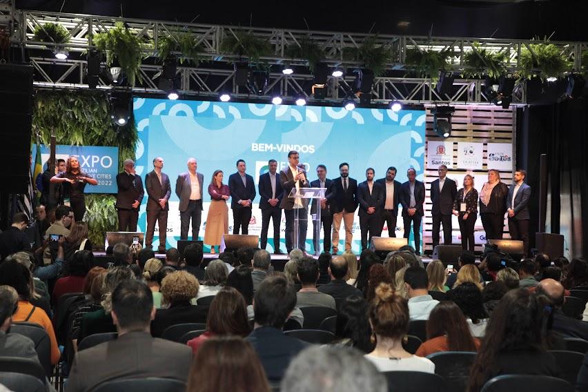 autoridades no palco do evento e grande público sentado. #paratodosverem