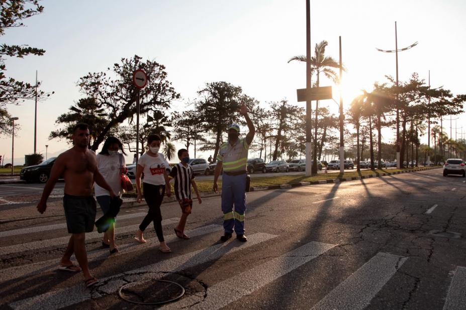 agente da CET está sobre a faixa e faz sinal para veículos. Pessoas atravessam a rua. #paratodosverem