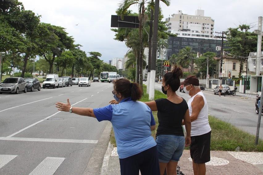 agente da CET faz sinal da faixa viva com o braço estendido e orienta dois pedestres em canteiro central na avenida. #paratodosverem
