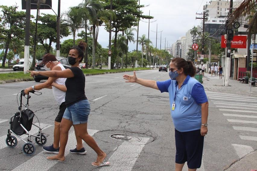 agente da CET estende o braço demonstrando a uma mulher e a um idoso como fazer para atravessar com segurança. #paratodosverem