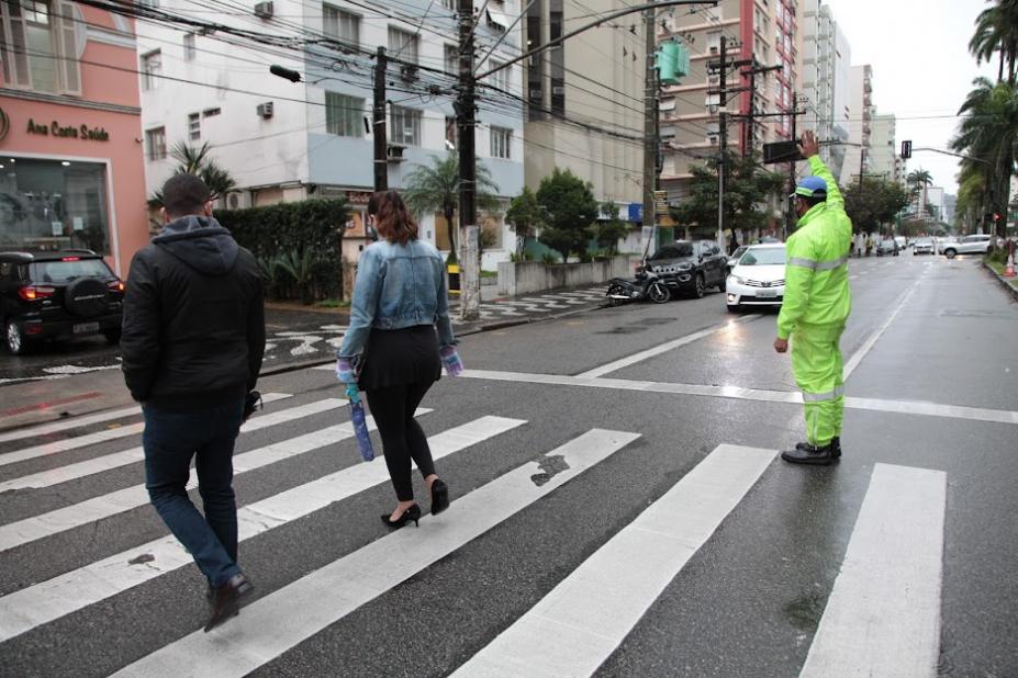 Agente sinaliza para motorista parar carro, enquanto pedestres atravessam na faixa. #pracegover