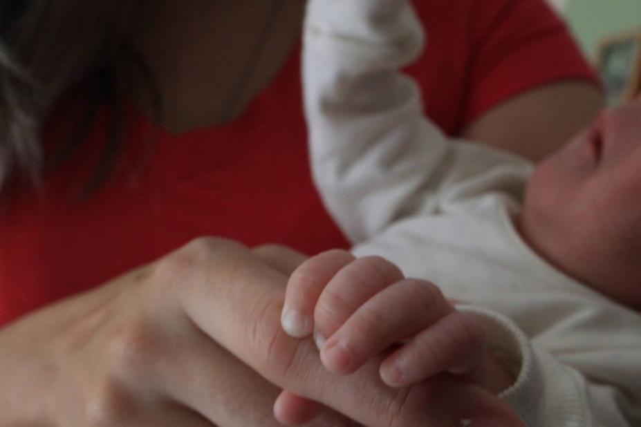 bebê está no colo de uma mulher. mãozinha do bebê está segurando um dedo dessa mulher. foto em close. #paratodosverem