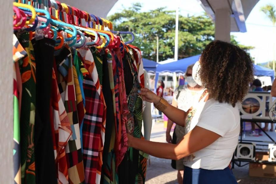 mulher mexe em roupas penduradas em arara em local aberto. #paratodosverem