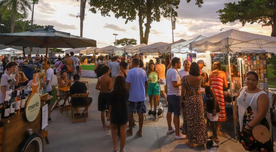 pessoas circulam em praça onde estão montadas barracas com exposição de peças artesanais. #paratodosverem