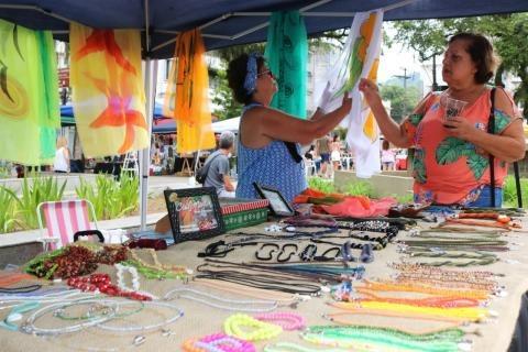 estande de venda com produtos expostos e duas mulheres mexendo em produtos. #paratodosverem