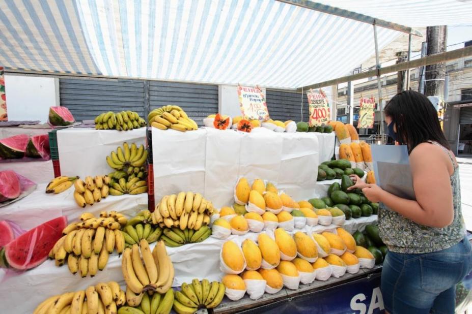 Mulher escolhe frutas em barraca da feira. #paratodosverem