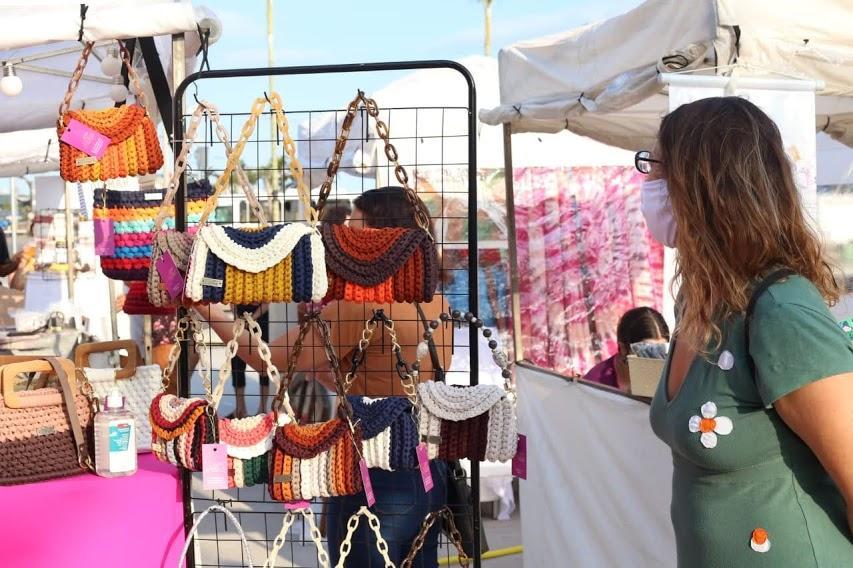 Mulher observa bolsas penduradas em barraca. #paratodosverem