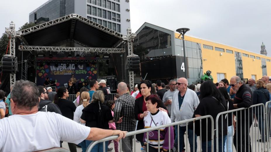banda toca no palco e pessoas passam na frente e acompanham #paratodosver