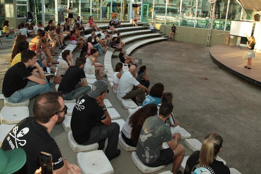 Público sentado na concha acústica assiste palestrante mulher. #pratodosverem