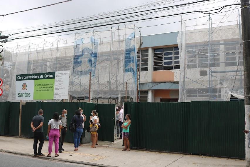 visitantes estão parados em porta de escola coberta por manta de proteção porque a fachada está em obras. #paratodosverem