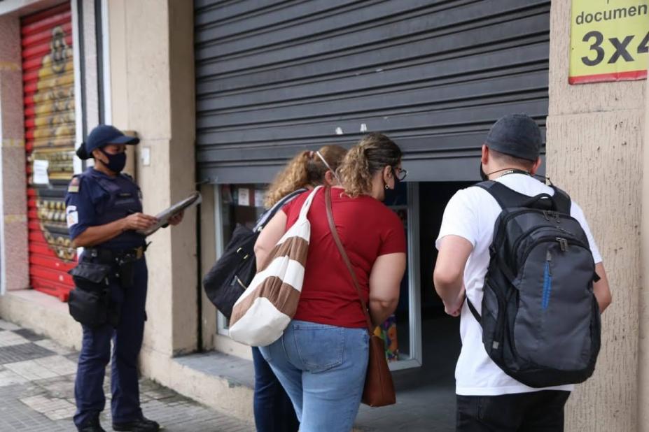 Guarda municipal e fiscais estão  na frente de um estabelecimento com porta semi-aberta. #Paratodosverem