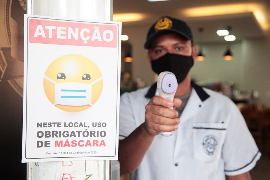 Homem usando máscara está segurando termômetro de testa.  Ele posa para a foto. #Paratodosverem