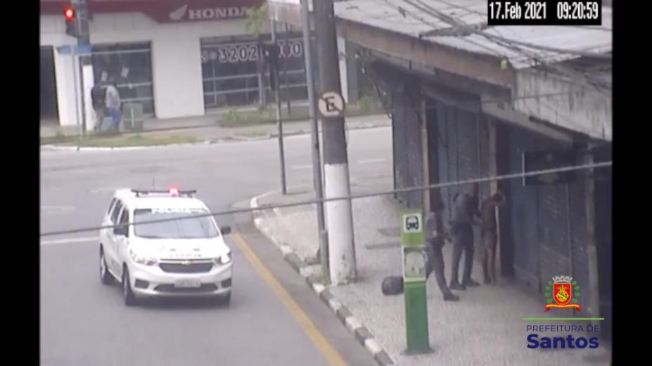 Viatura da polícia parada no meio da rua. Policiais revistam home na calçada. #Paratodosverem