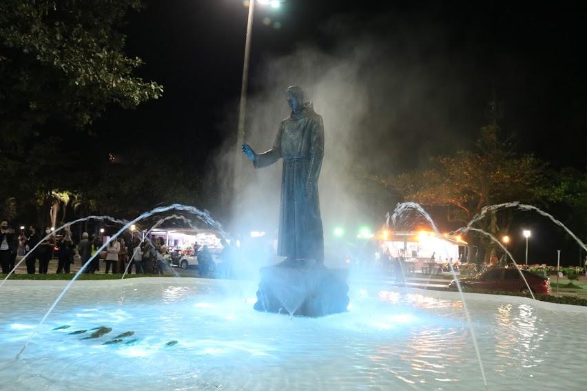 Fonte iluminada com a estátua de Santo Antônio ao centro. #pratodosverem