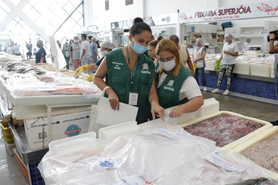 Duas fiscais observam caixas de isopor com pescados. #Paratodosverem