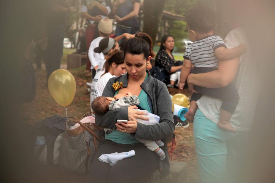 mãe alimenta bebê com bexiga ao lado #pracegover 