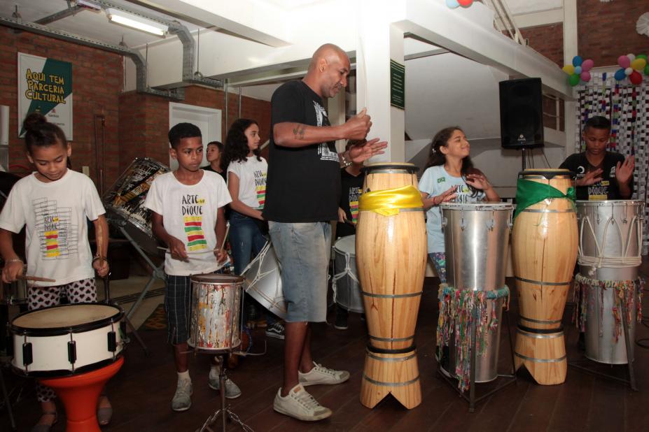 Jovens e um adulto fazem apresentação de percussão. #Pracegover