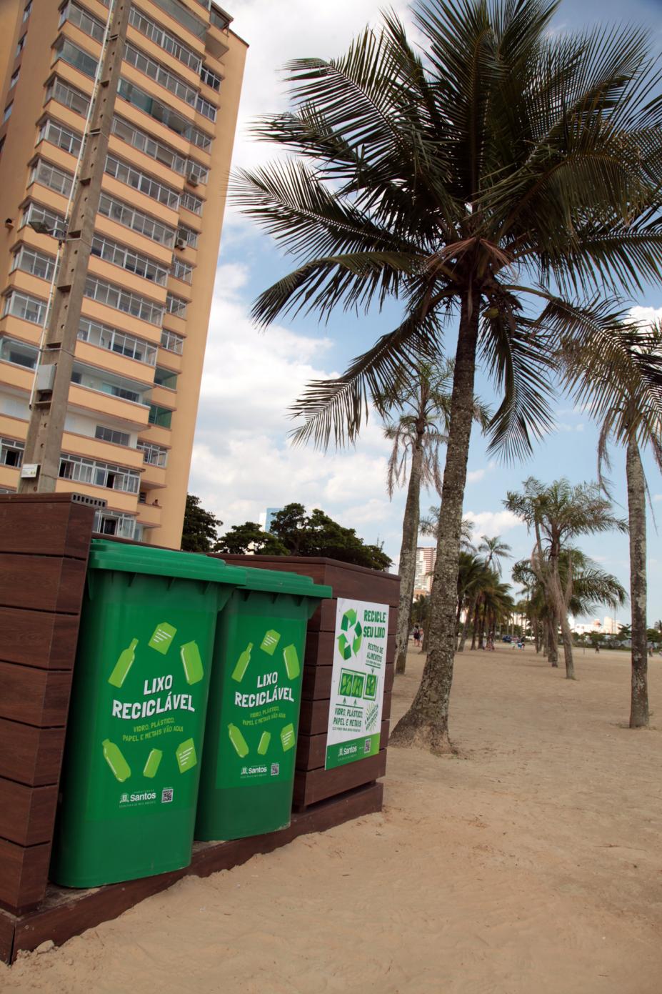 Novos contentores posicionados sobre a areia da praia. Ao fundo aparece um prédio e algumas palmeiras. #Pracegov