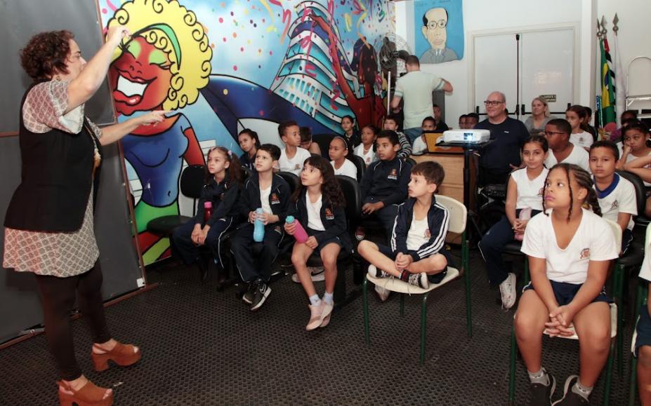 crianças estão sentadas em auditório assistindo palestra. #paratodosverem