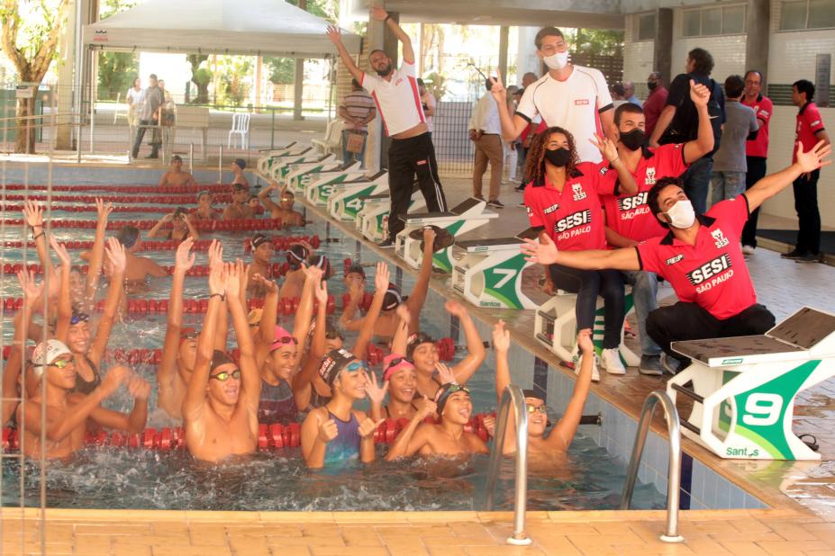 pessoas dentro de uma piscina com as mãos para cima , fora da piscina pessoas com braços abertos #paratodosverem