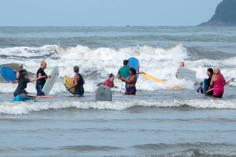 pessoas maduras entram no mar com pranchas. #paratodosverem 