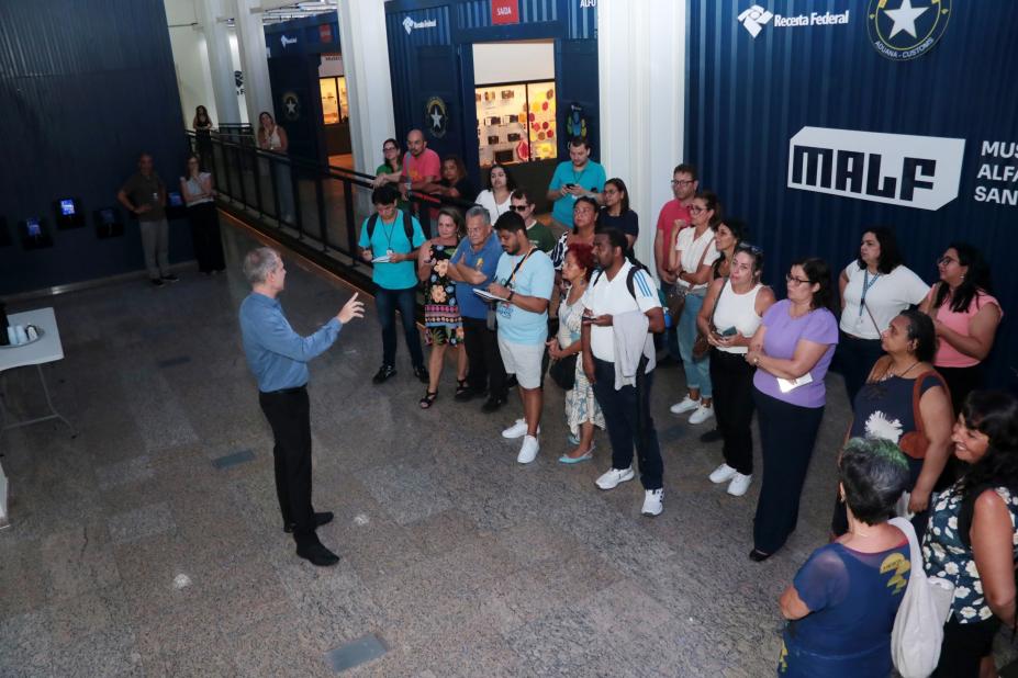 grupo de pessoas assiste homem falando dentro de museu. #paratodosverem 