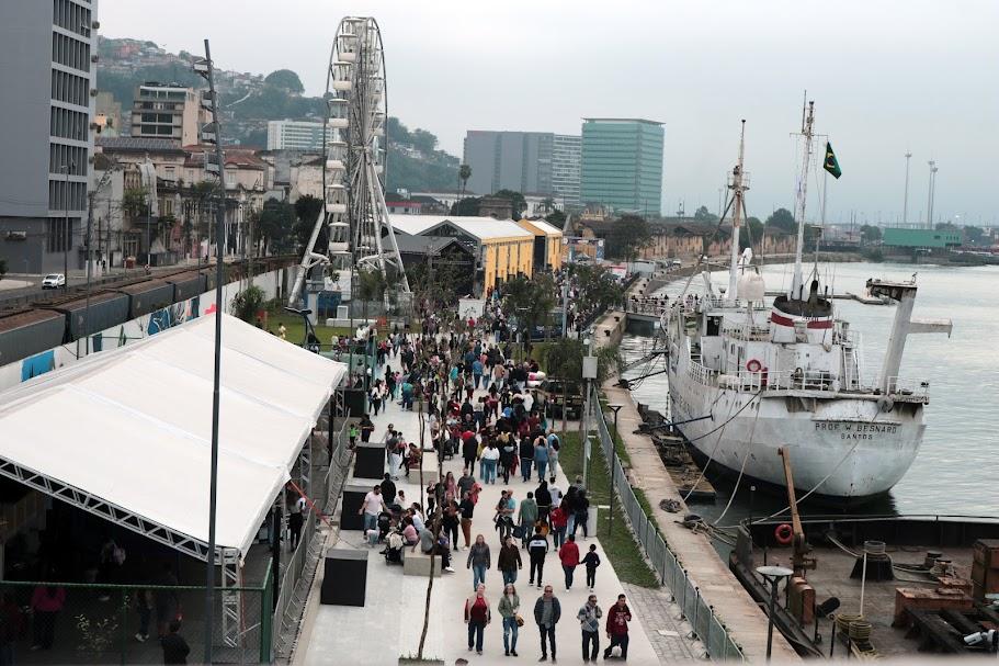 vista aérea geral do parque valongo, com o mar à direita e a roda gigante ao fundo. Pessoas circulam pelo local. #paratodosverem 