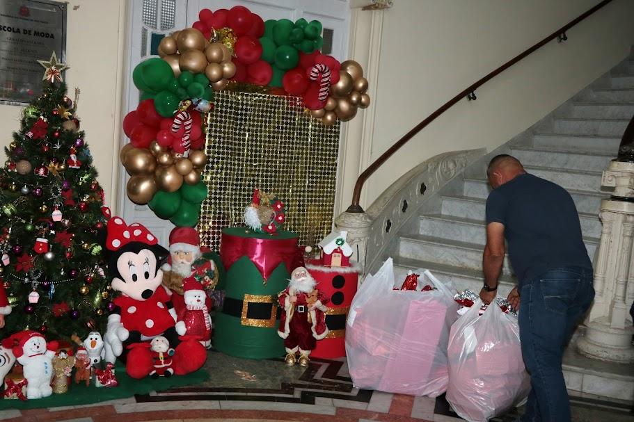 salão com decoração de natal e um homem de costas para a foto acomodando dois grande sacos com presentes. #paratodosverem 