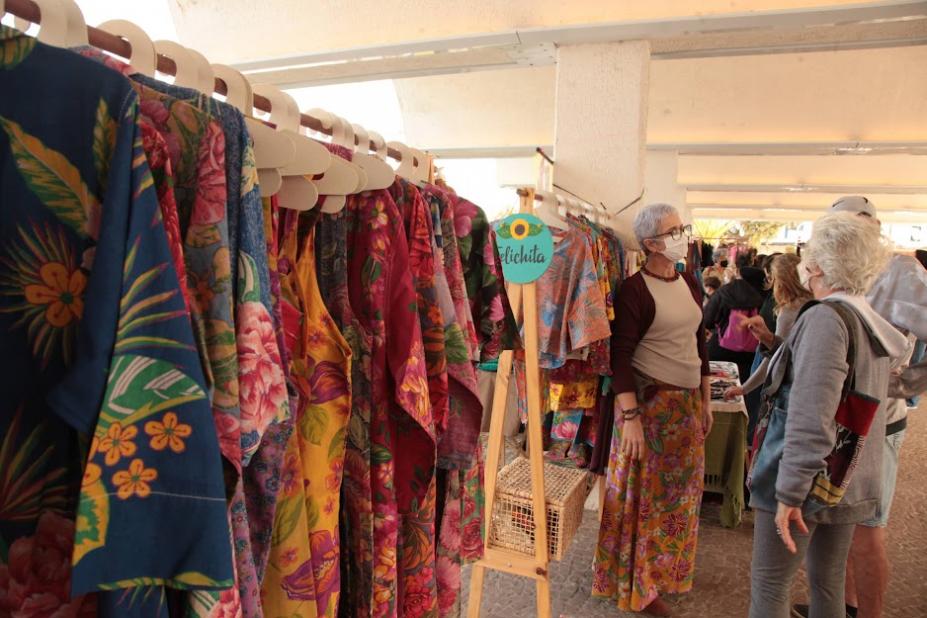 roupas coloridas penduradas em arara em ambiente de feira criativa. #paratodosverem 