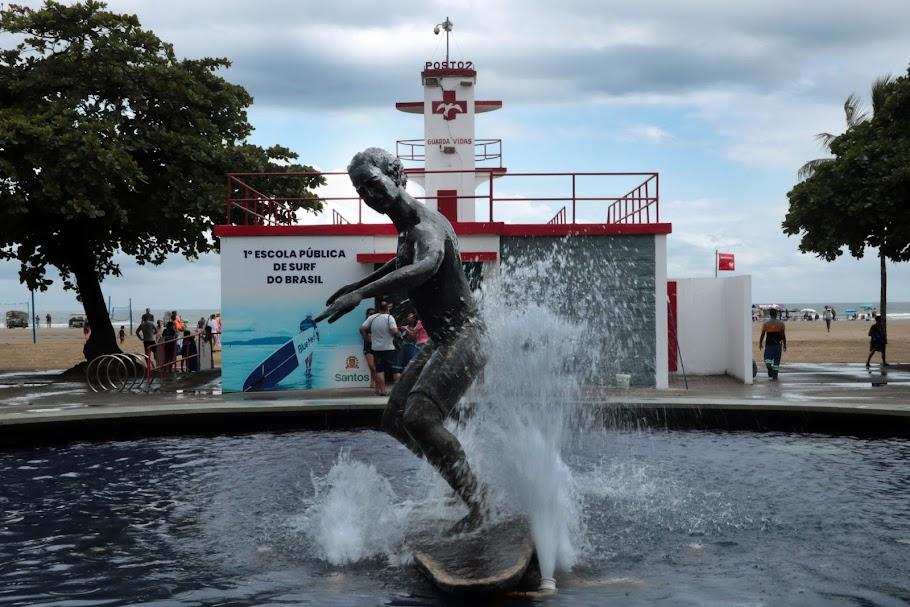 a fachada da escola de surfe com a estátua de surfista na água em primeiro plano. #paratodosverem 